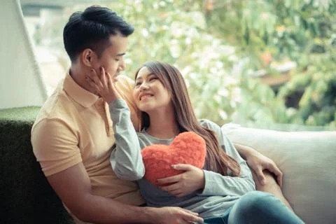 Asian Couples Sitting on the sofa In which women Holding a red heart And smil Stock Photos