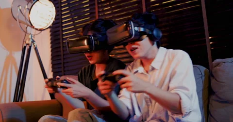 Asian couples wearing modern Virtual reality glasses sit use joystick play games Stock Footage 164660838