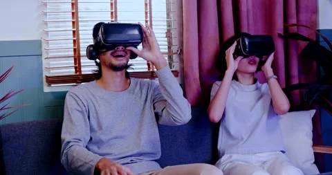 Asian couples wearing modern Virtual reality glasses sit use joystick play games Stock Footage 171377830