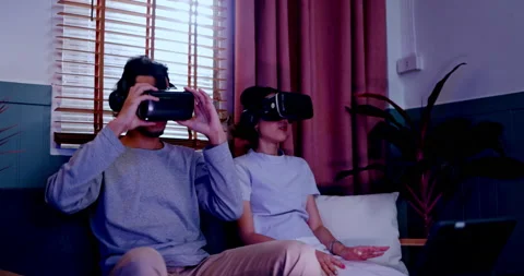 Asian couples wearing modern Virtual reality glasses sit use joystick play games Video stock 171378141