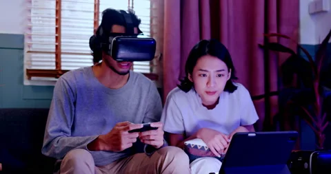 Asian couples wearing modern Virtual reality glasses sit use joystick play games Vidéo 171378222