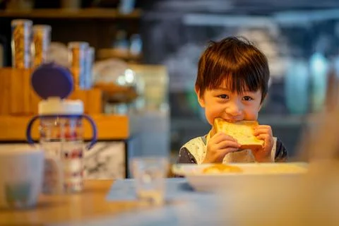 Asian cute boy show his teeth to biting big toast. Little child, caucasian bo Stock Photos