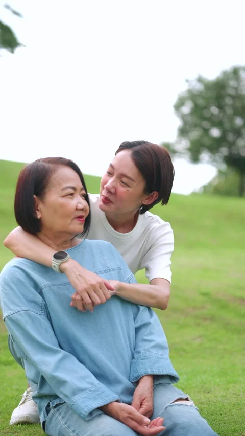 Asian daughter lovingly embraces her mother from behind in a green park. Stock Footage 346509729
