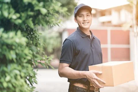 Asian delivery man smiling while holding a cardboard box Stock Photos