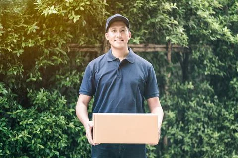 Asian delivery man smiling while holding a cardboard box Stock Photos