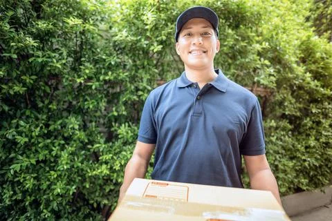Asian delivery man smiling while holding a cardboard box Stock Photos