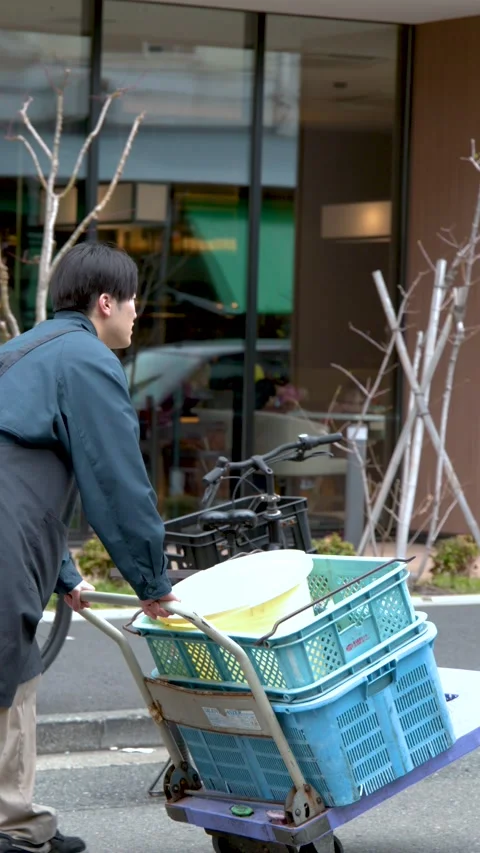 Asian Delivery Worker Pushing Hand Truck with Blue Crates in Tokyo Stock Footage 342494297