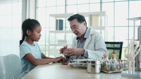 Asian dentist explains the tooth model to Black patient girl in dental clinic. Stock-Footage 329739893