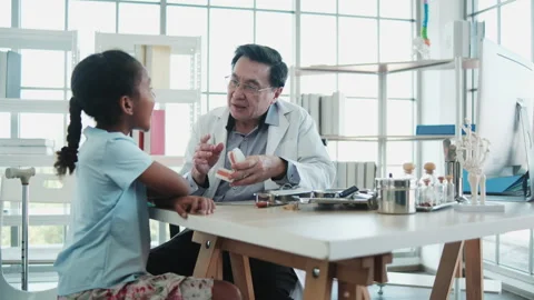 Asian dentist explains the tooth model to Black patient girl in dental clinic. Stock Footage 332472703