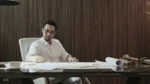 Asian designer sitting behind table contemplating and sketching Stock Footage 160943732