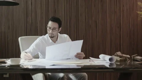 Asian designer sitting behind table contemplating and sketching Stock Footage 160943741