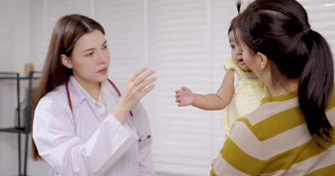 Asian doctor smiling while talking to toddler in mother’s arms during clinic Stock Footage 322087721