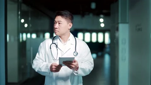 Asian doctor uses a tablet computer while standing in a modern hospital clinic.  Stock Footage 166235975