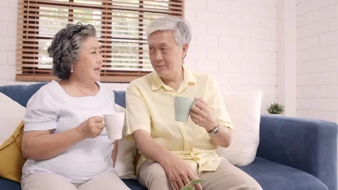 Asian elderly couple drinking warm coffee and talking together in living room. Stock Footage 104772976