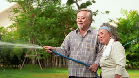 Asian elderly couples are using rubber tube to water the plants in the backyard Stock-Footage 136754976