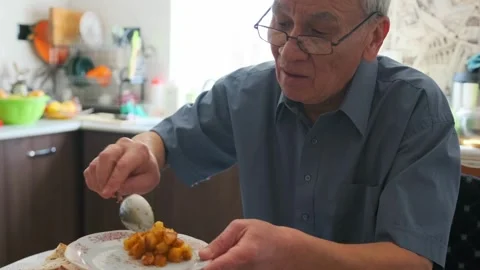 Asian Elderly Man Arranging Plate At Small Kitchen Table, Placing Bread And Sid Stock Footage 326866757