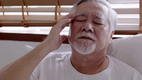 Asian Elderly man with a headache sitting on a bed in morning Stock Footage 153257576