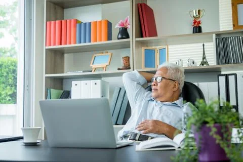 Asian elderly man sitting in front of a laptop computer, He is sitting back i Foto stock