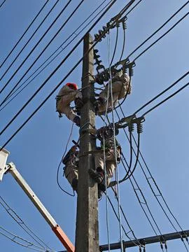 Asian electrical lineman worker team climbing high voltage concrete pole. Stock Photos