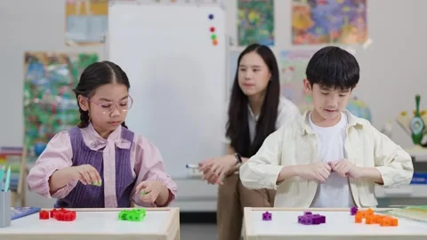 Asian Elementary Students Building with Toy Blocks in Classroom with Teacher Stock Footage 335617192
