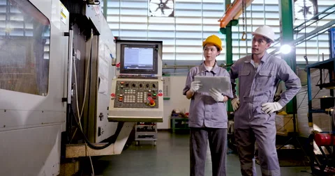 Asian engineer pair stands beside CNC machine with tablet, reviewing production Stock Footage 332906185