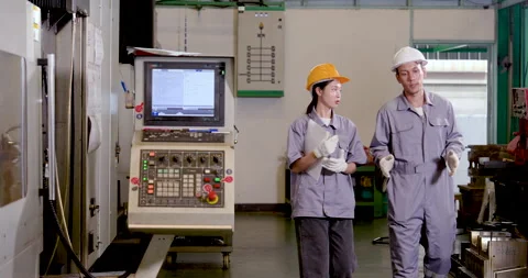 Asian engineer pair walks beside CNC machine and control panel, discussing Stock Footage 338071221