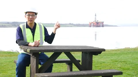 Asian engineer sitting on the desk in front of semi submersible oil rig Stock Footage 63121235