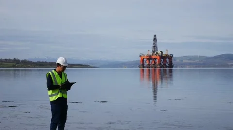 Asian engineer standing in front of semi submersible oil rig 63117593