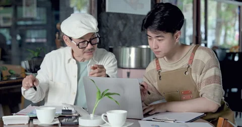 Asian father explains cafe management while son studies laptop, learning family Stock Footage 335561665
