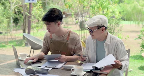 Asian father guides son using laptop and tablet at outdoor cafe table, Stock Footage 335561028