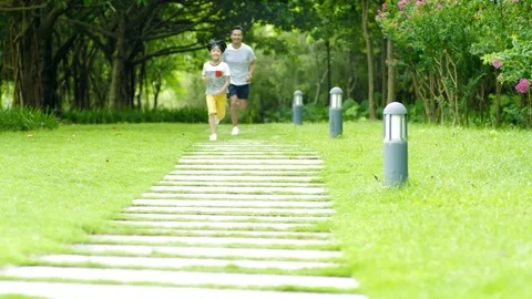 Asian father running behind his son in park in summer in slow motion Stock Footage 80459986