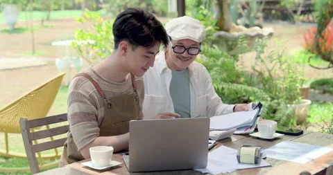 Asian father smiles while coaching son at outdoor cafe table, reviewing business Video stock 333455353