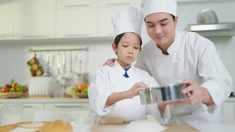 Asian father teaching son preparing dough, baking cookies wearing chef costume Stock-Footage 240068561