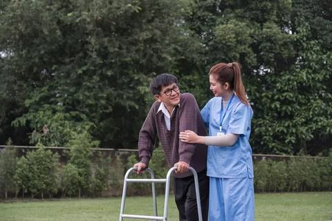 Asian female caregiver helps senior man walk A senior using a walker is assisted Stock Photos