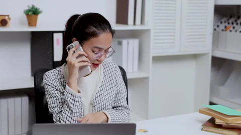 Asian female checking data from laptop while having phone call at home office Stock Footage 327453598