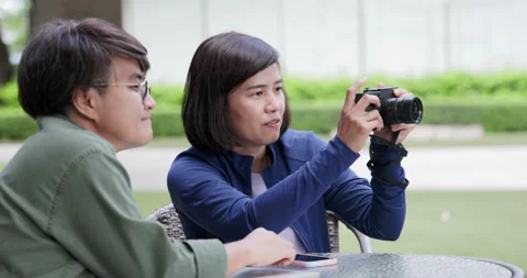 Asian female couple using mirrorless camera sit in park practicing photography Stock Footage 163661592