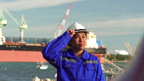 Asian female engineer adjusting hard hat while looking up at cargo ship Video stock 342919009