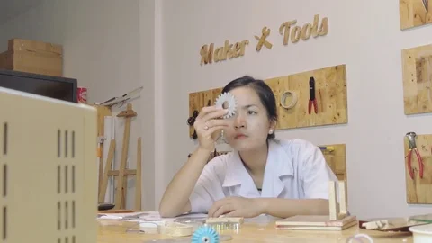 Asian female engineer looks closely at a gear in a maker lab (wide shot) Stock Footage
