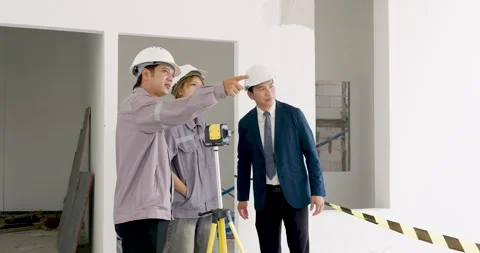 Asian female engineer points toward unfinished wall while male contractor and Stock Footage 342225247