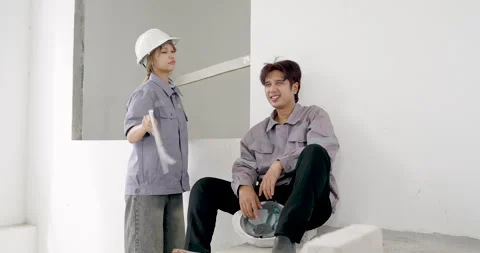Asian female engineer standing with blueprint instructs seated male worker Stock Footage 336536176