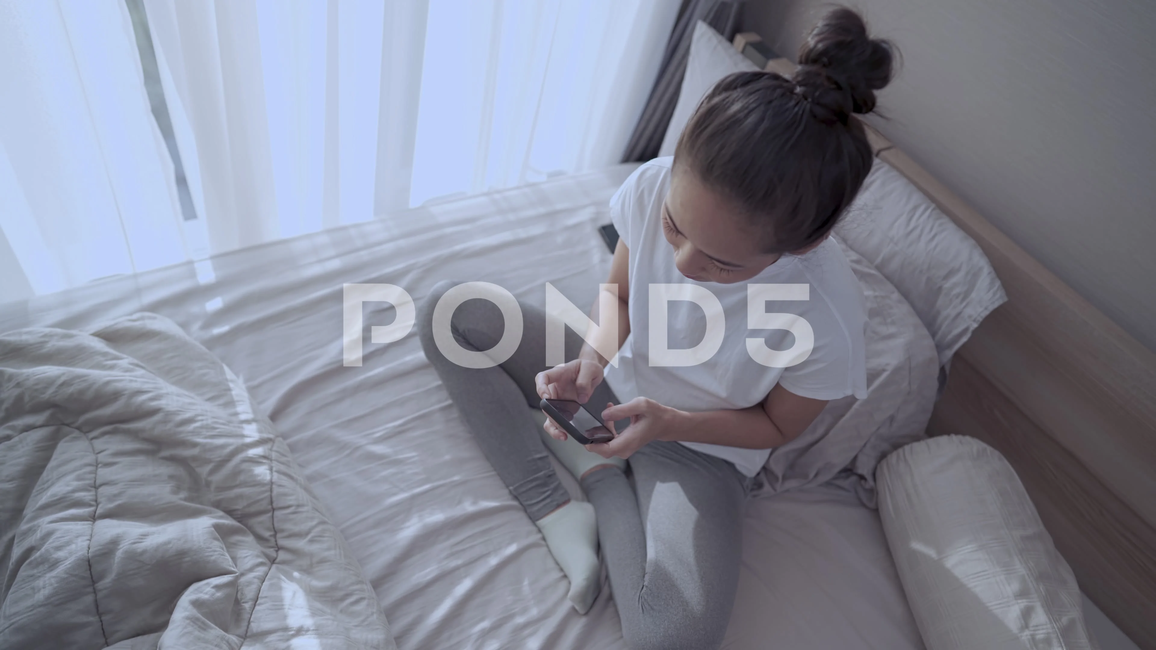 Asian female hair tied up sitting in the bedroom, Using cellphone to get  online