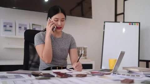 Asian female interior designer talking phone writing notes working on creat.. Stock Footage 333466938