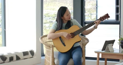 Asian female looking at tablet, strumming and fretting guitar while practicing Stock Footage 335000055