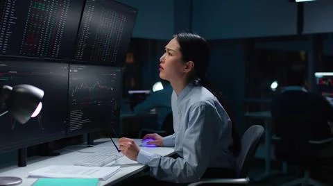 Asian female programmer staring at computer monitors with data Stock Photos