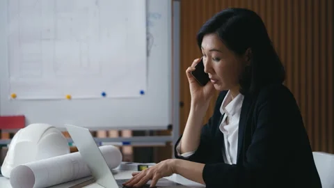 Asian female property developer talks on her phone while working in her office Stock Footage 302468419