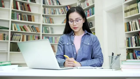 Asian female student having learning difficulties using laptop taking notes  Stock Footage 274142768