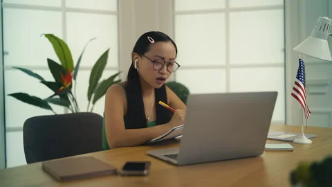 Asian female student making notes during online English language class on laptop Stock Footage 310736136