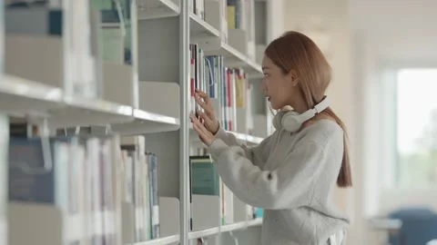 Asian Female student taking notes from a book at library. Young asian woman sitt Stock Footage 220895045
