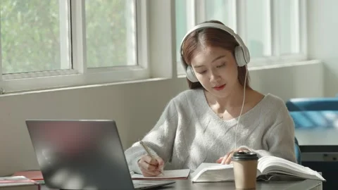Asian Female student taking notes from a book at library. Young asian woman sitt Stock Footage 220896546