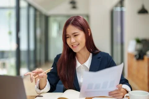 Asian female worker using computer and budget documents on desk Stock Photos